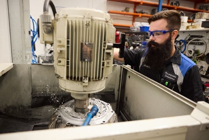 Technician operating a CNC milling machine while machining a metal powertrain part in an industrial workshop.